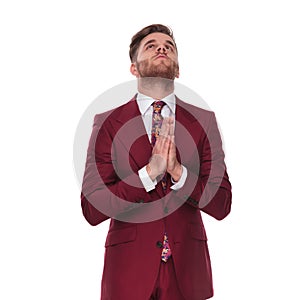 Young businessman in grena suit praying and looking up