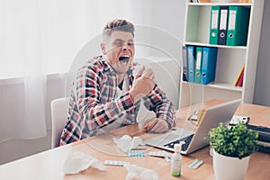 Young businessman with grippe working on laptop and sneezing in napkin photo