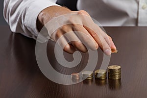 Young businessman hand holding a coin with row stacks