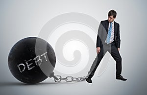 Young businessman has chained big metal ball to his leg with debt written.