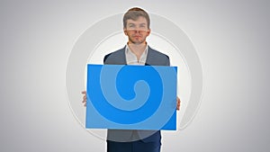 Young businessman holding blank sign looking at camera on gradie