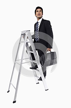 Young businessman holding a briefcase, climbing a ladder. Conceptual image