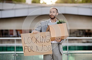 Young businessman holding cardboard sign with the text LOOKING FOR A JOB