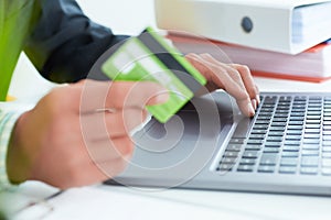 Young businessman holding a credit card and typing. On-line shopping on the internet using a laptop. Just hands over the