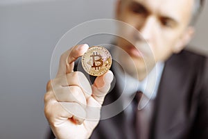 Young businessman holding in hand symbol of bitcoin crypto currency - electronic virtual money for web banking. Shallow depth of f