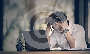 Young businessman holding his head while working on laptop