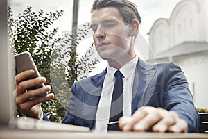 Young businessman holding mobile phone in hand and looking at screen.