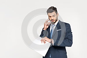 young businessman holding papers and talking on smartphone while checking wristwatch
