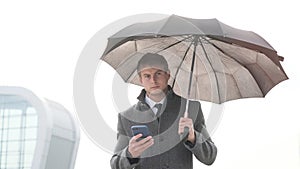 Young businessman holding umbrella and using a smart phone in a