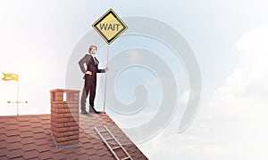 Young businessman on house brick roof holding yellow signboard.
