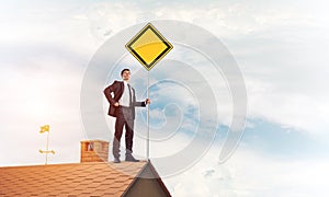 Young businessman on house brick roof holding yellow signboard.