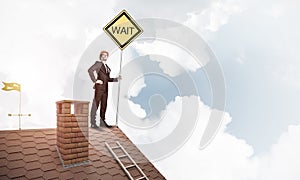 Young businessman on house brick roof holding yellow signboard.