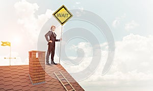 Young businessman on house brick roof holding yellow signboard.