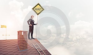 Young businessman on house brick roof holding yellow signboard.