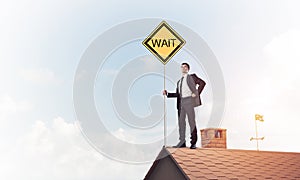 Young businessman on house brick roof holding yellow signboard.