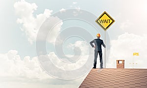 Young businessman on house brick roof holding yellow signboard.