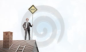 Young businessman on house brick roof holding yellow signboard.