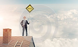 Young businessman on house brick roof holding yellow signboard.