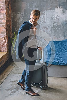 young businessman with jacket over shoulder carrying suitcase in bedroom