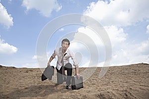 Young businessman kneeling in the desert and holding a briefcase, exhausted