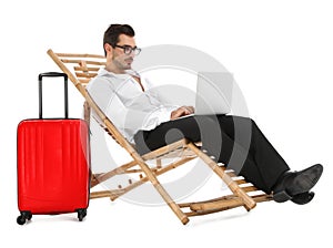 Young businessman with laptop and suitcase on sun lounger against white background