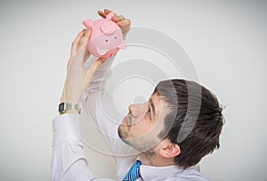 Young businessman is looking in empty piggy money bank