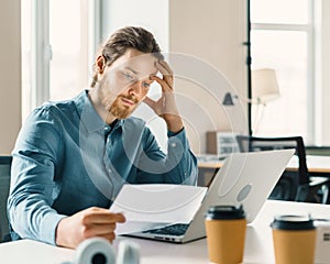 Young businessman looking at financial document or bill with frustrated expression