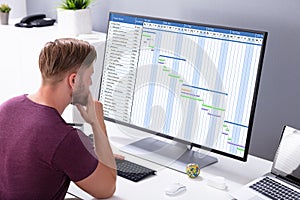 Young Businessman Looking At Gantt Chart On Computer In Office