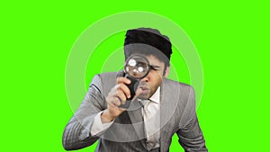 Young businessman looking through a magnifying glass on green background