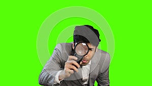 Young businessman looking through a magnifying glass on green background