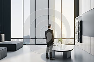 Young  businessman looking out of window in modern office room interior. Future, tomorrow and executive concept