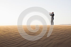 Young businessman looking through telescope in the middle of the desert