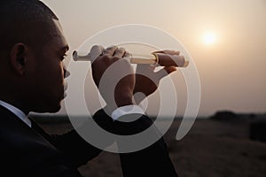 Young businessman looking through telescope in the middle of the desert