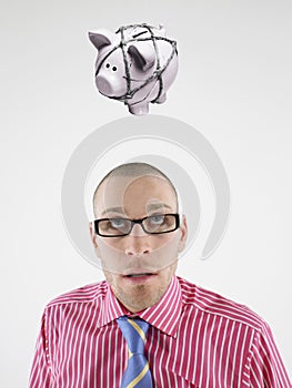 Young businessman looking up at piggy bank tied with rope representing trapped finances