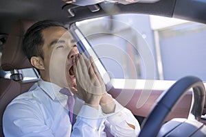 Young businessman looks tired yawning while driving the car