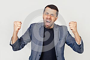 Young businessman man with a beard angry and insane, raising his fists, frustrated and furious, screaming in anger. Rage and