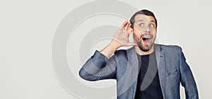 Young businessman man with a beard in a jacket, smiling with his hand above his ear, listening to rumors or gossip. Deafness