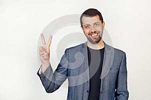 Young businessman man with a beard in a jacket, smiling, looking at the camera, showing thumbs up, making a victory sign. Number