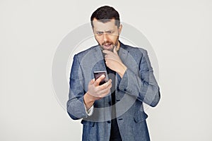 Young businessman man with a beard in a jacket using a smartphone scared shocked with a surprised face, scared and excited with an
