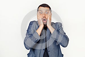 Young businessman man with a beard scared and shocked, surprised and surprised with hands on his face. Portrait of a man on a gray