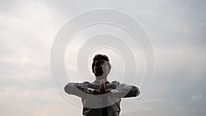Young businessman meditating under grey sky