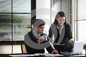 Young businessman in a meeting with an attractive female colleague discussing information on a laptop at office.