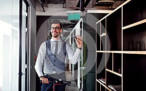 Young businessman with scooter in an office building, waving at somebody. photo