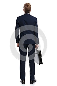 Young businessman in navy blue suit holding suitcase and looking up