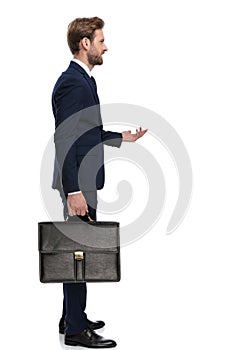 Young businessman in navy blue suit holding suitcase and standing in line