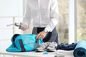 Young businessman packing sports stuff for training into bag