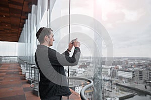 Young businessman photographing a city on the phone with a skyscraper.