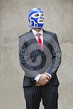 Young businessman in pinstripes suit and wrestling mask looking away over gray background photo