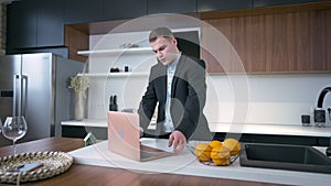Young businessman placing bowl with fruits on tabletop surfing Internet on laptop in slow motion. Portrait of serious