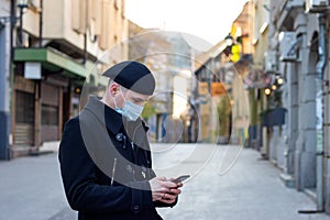 Young businessman with protective mask on face standing alone on empty street.